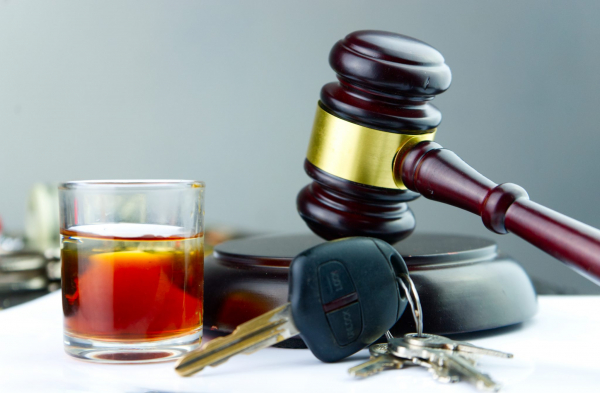 A glass of liquor, a gavel, and a se too car keys on a table.